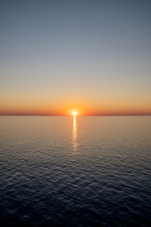 Free A peaceful sunset over the ocean, casting a golden reflection on the water. Stock Photo