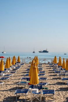 A serene beach scene with yellow umbrellas and lounge chairs overlooking calm sea waters.