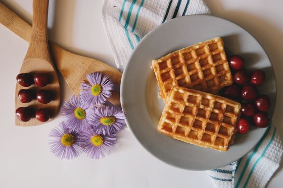 Two square golden waffles on a gray plate surrounded by fresh dark red cherries