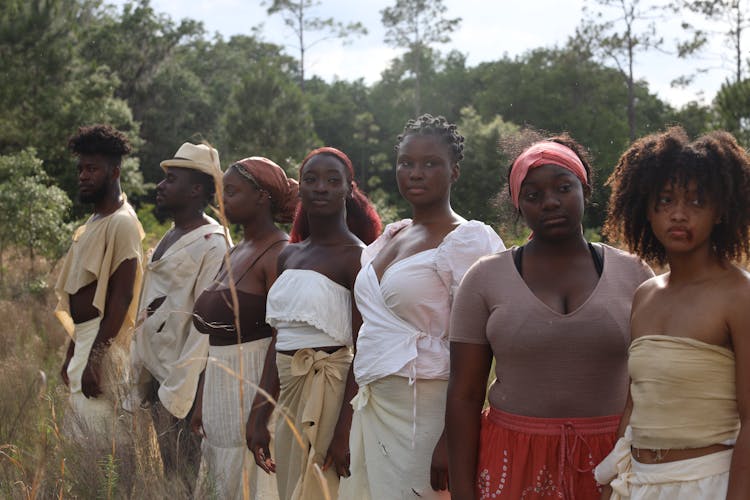 A Group Of Serious People Standing On Brown Grass 