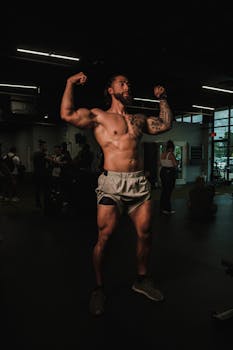 Muscular man flexing in a gym, showcasing tattoos and fitness.