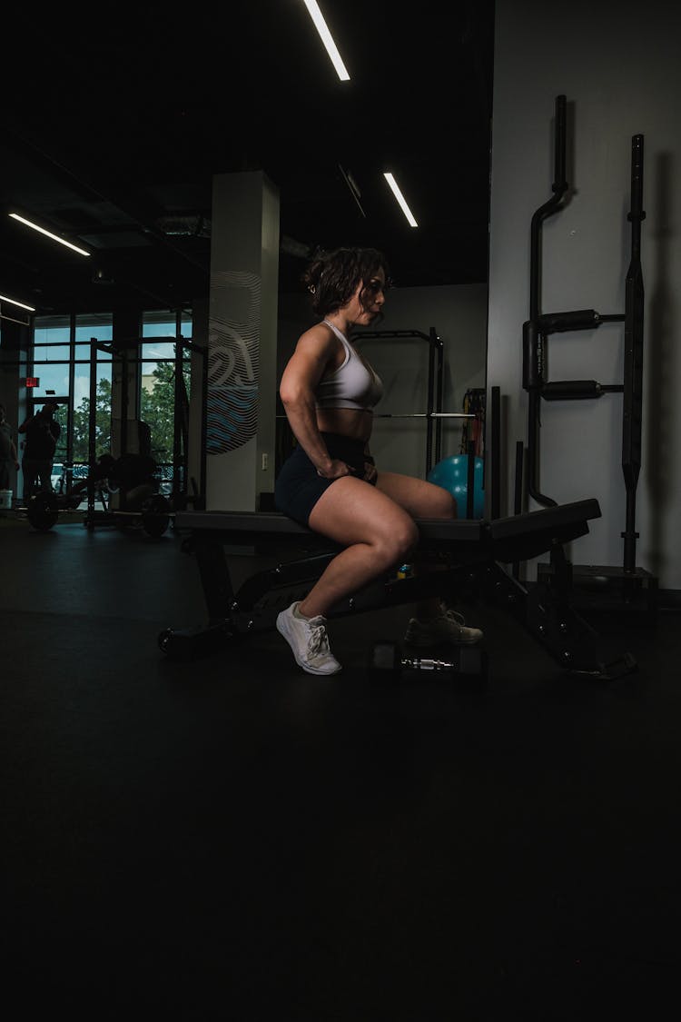 A Woman Sitting On A Bench In A Gym