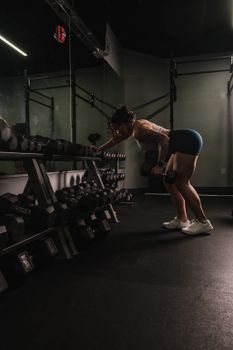 A woman performs a bent-over row with dumbbells in a gym, exemplifying strength and fitness.