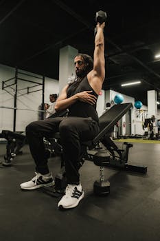 Man lifting dumbbell at gym, focusing on strength training in modern fitness environment.