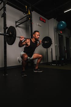 Adult male engaging in barbell squats, showcasing strength training in a gym environment.