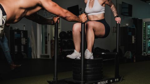 Energetic couple engaged in intense strength training with gym sled indoors.