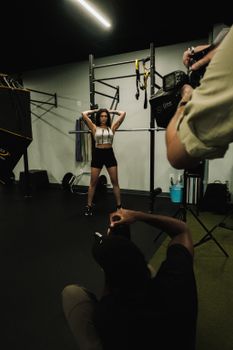 A woman in sportswear posing confidently during a fitness photoshoot in a gym setting.