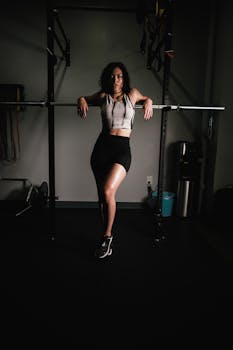 Woman in activewear posing with barbell in gym, highlights strength and style.