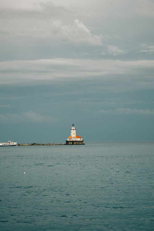 Free A tranquil seascape featuring a lone lighthouse under a soft cloudy sky. Stock Photo
