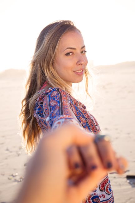 A smiling woman enjoying a sunny day at the beach, holding hands and looking back.