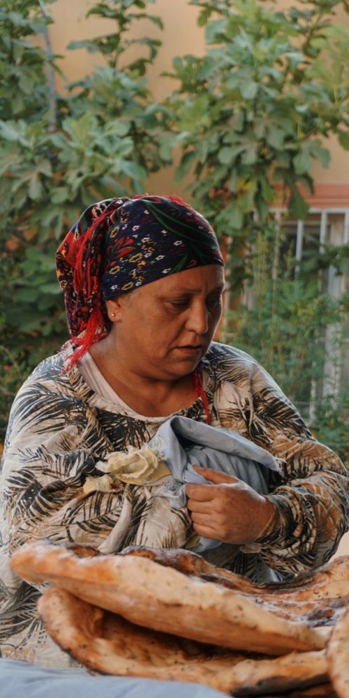 Free Middle-aged woman with headscarf handling bread at an outdoor market in Türkiye. Stock Photo