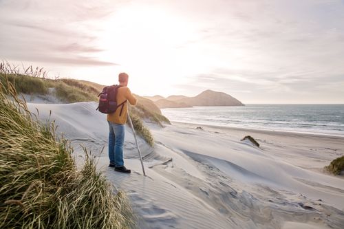 Free A lone hiker explores sand dunes by the ocean at sunrise, capturing nature's beauty. Stock Photo