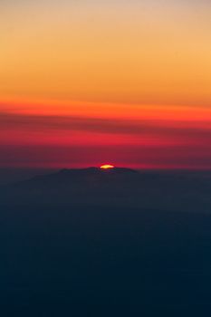 Vivid sunset with striking orange and red hues over a silhouetted mountain horizon.