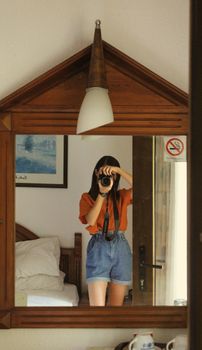 Woman in denim shorts taking a photo in a mirror, capturing a cozy room setting.