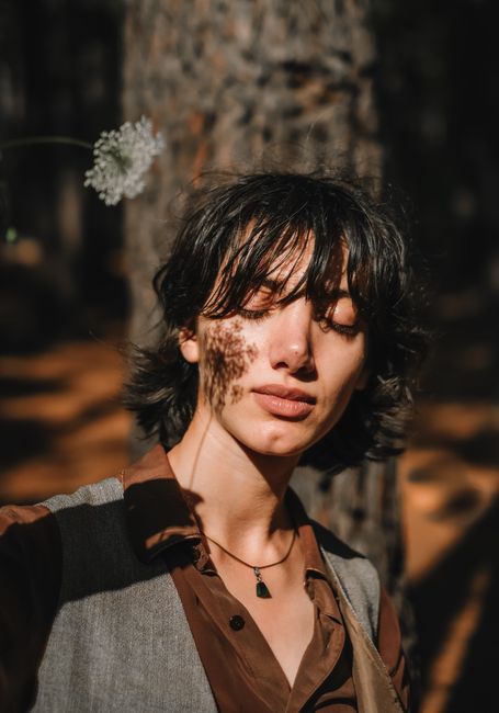 Close-up portrait of a woman outdoors with a flower shadow casting on her face, eyes closed.