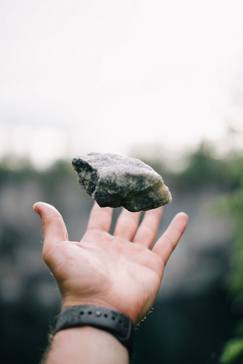 Faceless man throwing stone on hand outdoors