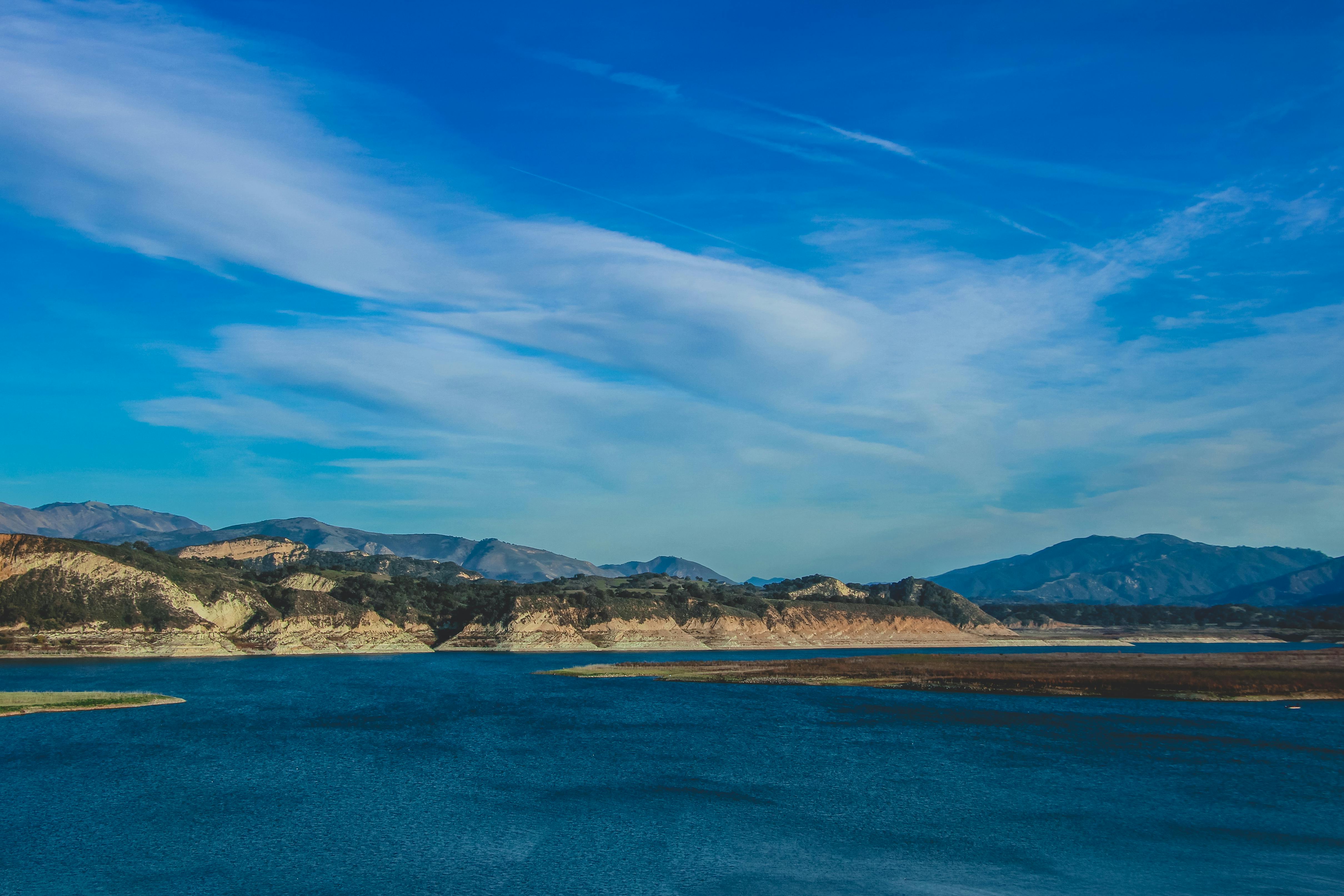 Blue Ocean near Mountains under the Cloudy Blue Sky · Free Stock Photo