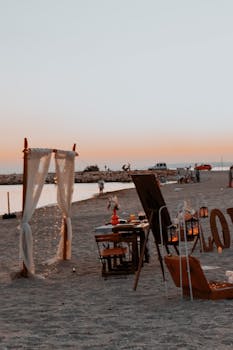 A scenic beach dinner arrangement with chairs and table at sunset, ideal for romantic occasions.
