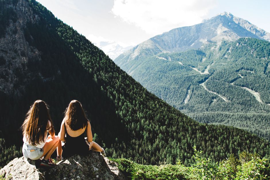 Two women sitting on a cliff overlooking the scenic Valsavarenche mountains in Aosta, Italy.