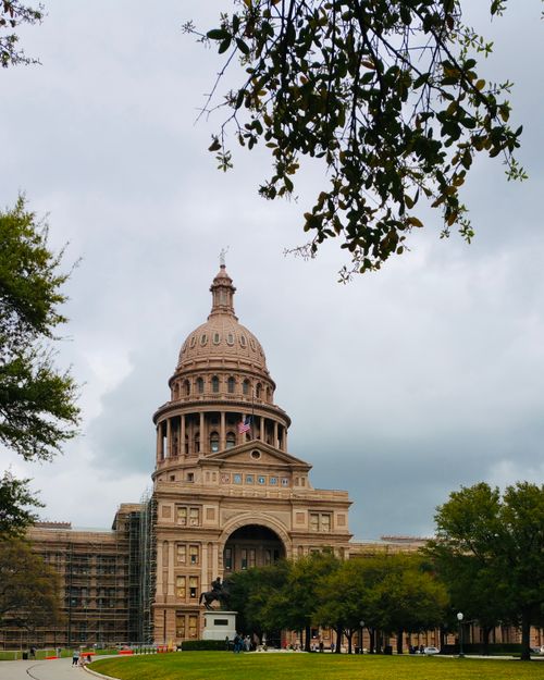 Free Historic Texas State Capitol building framed by trees under a cloudy sky in Austin. Stock Photo