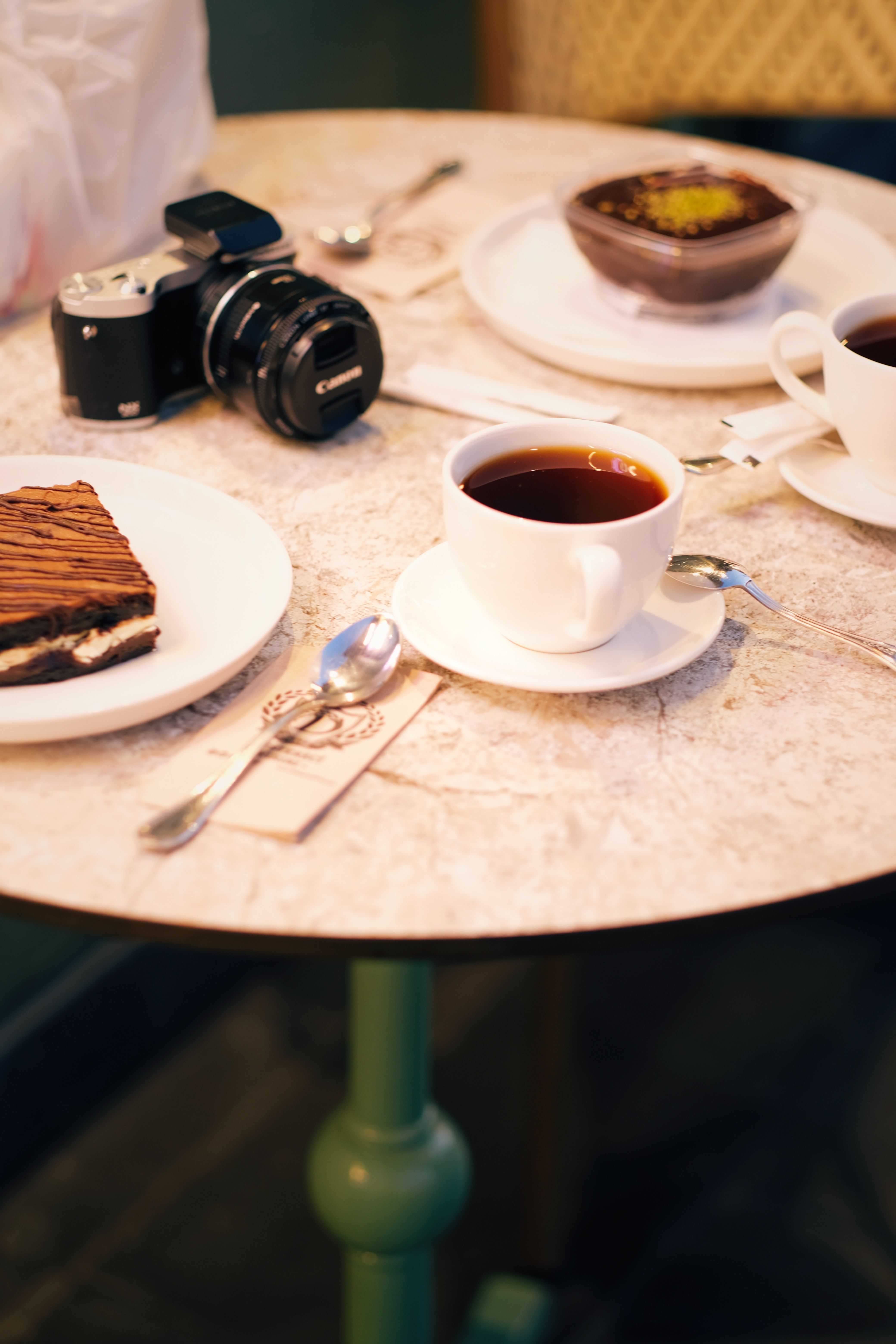 Warm café ambiance with black coffee, dessert, and vintage camera on a marble table.