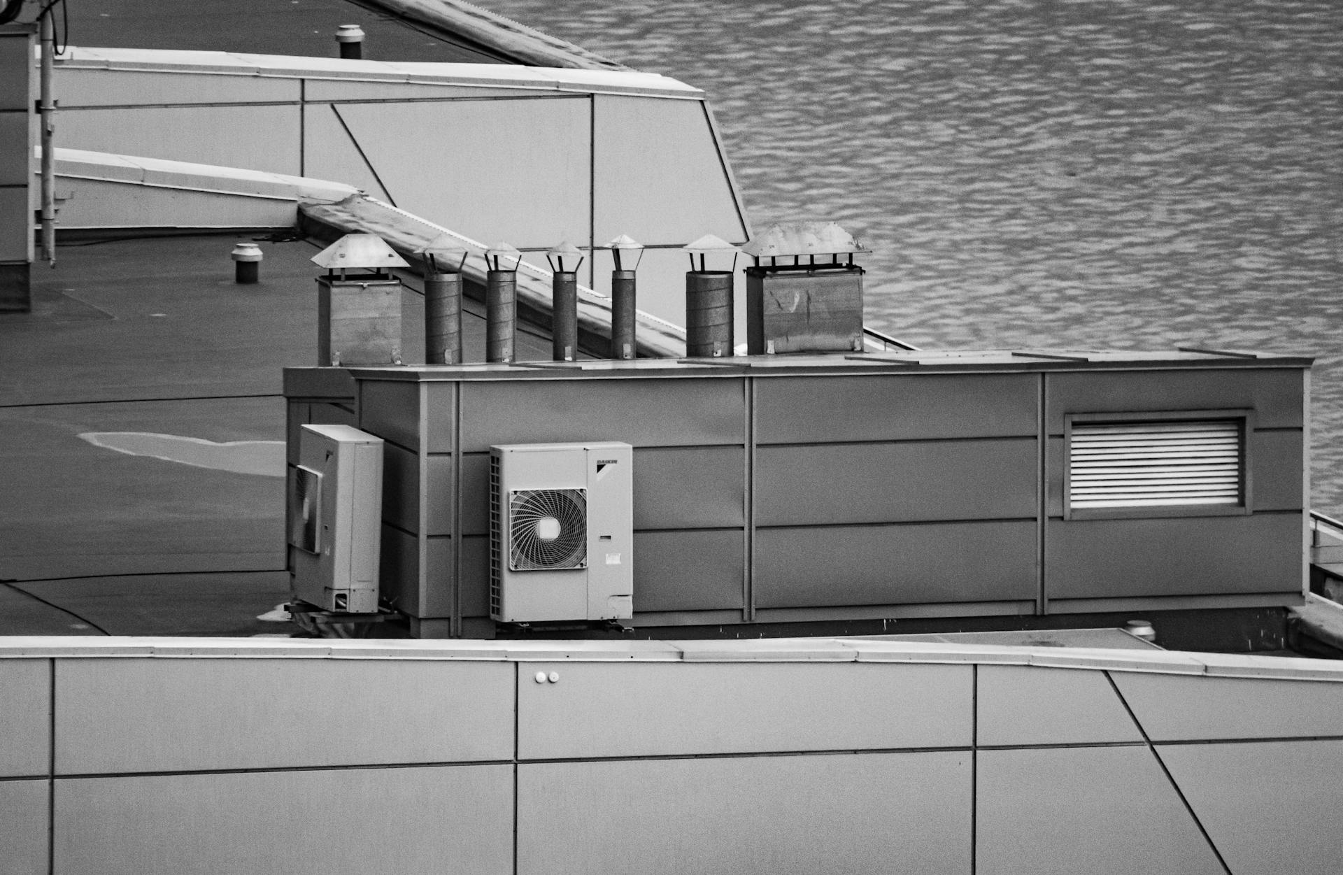 Black and white image showcasing a modern rooftop with air conditioning and ventilation units by the waterfront.