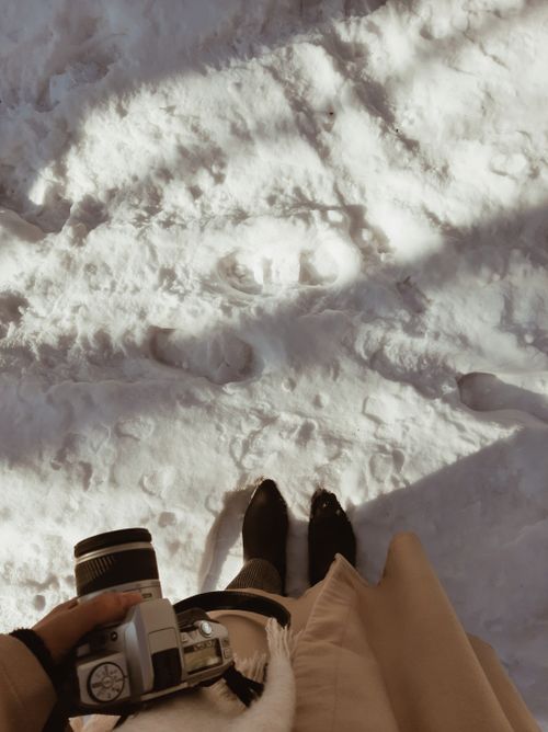 Free A person holding a camera standing in snow, capturing a winter perspective. Stock Photo