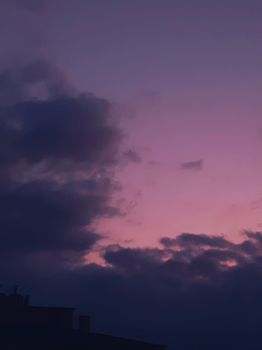 Capture of a purple sky at dusk with clouds and a crescent moon.