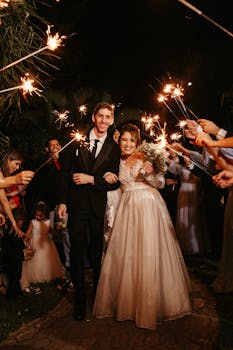 A joyful wedding night with newlyweds walking under sparklers, surrounded by guests.