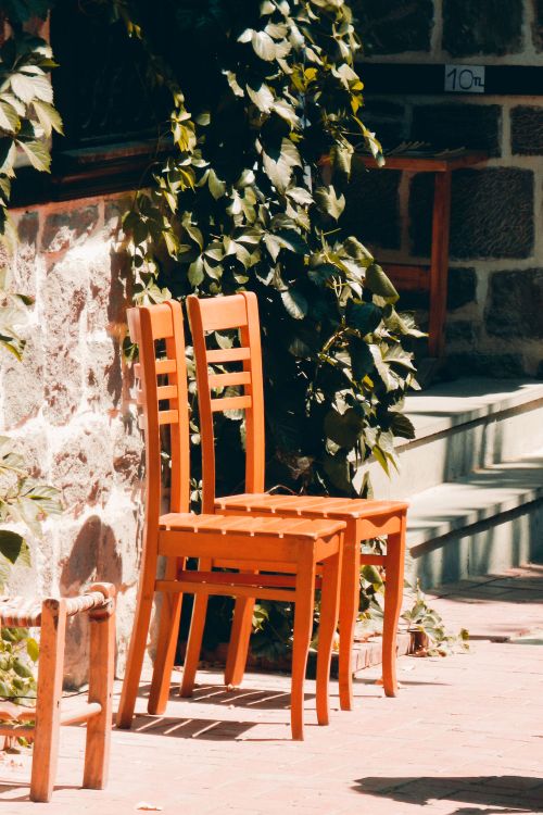 Free Two orange wooden chairs beside an ivy-covered stone wall in sunlight. Stock Photo