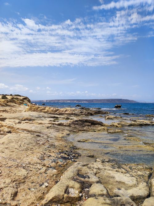 Free Scenic view of a rocky shoreline meeting a calm blue sea under a bright sky. Stock Photo