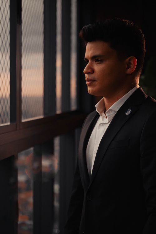 Free A contemplative businessman in a suit looks out a window at sunset, conveying ambition and reflection. Stock Photo