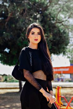 Fashionable woman with long hair poses outdoors against a natural backdrop, exuding elegance and modern style.