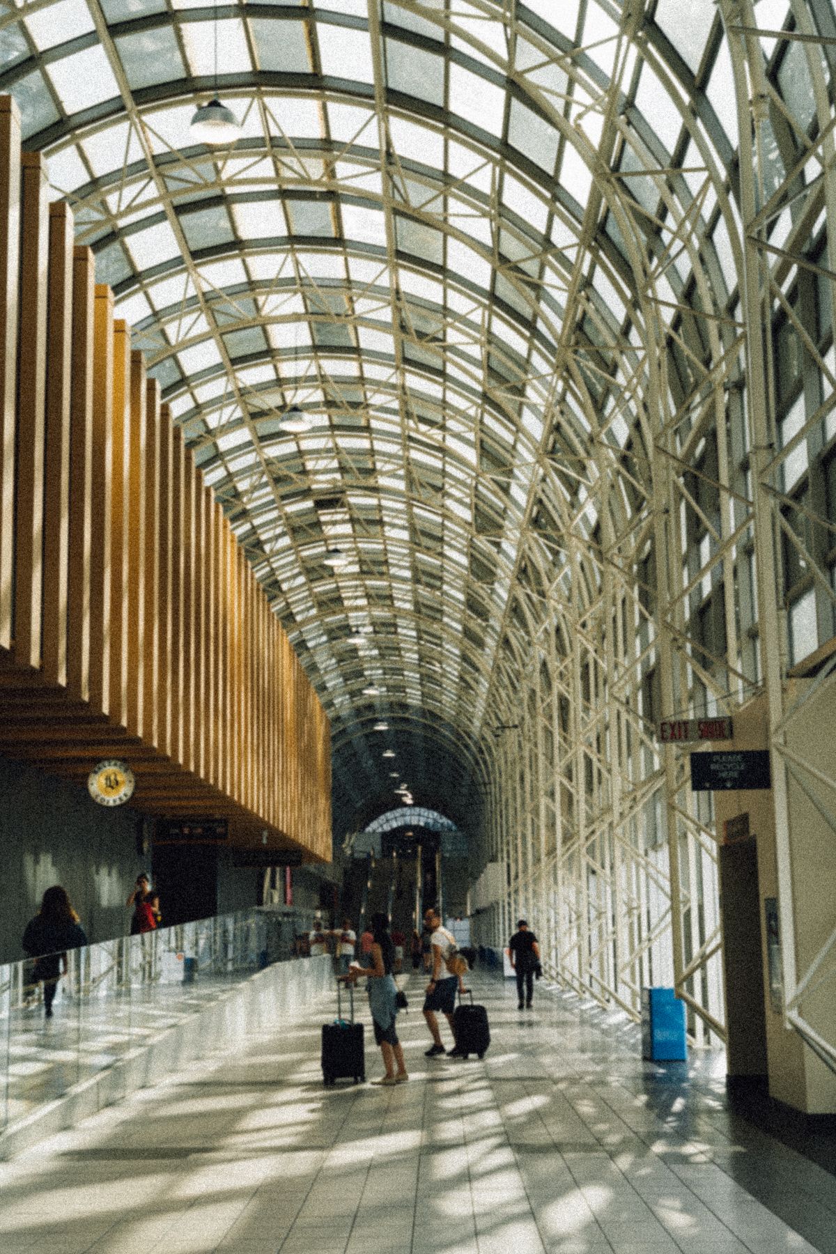 Travellers pulling suitcases through a sunlit airport arrivals corridor