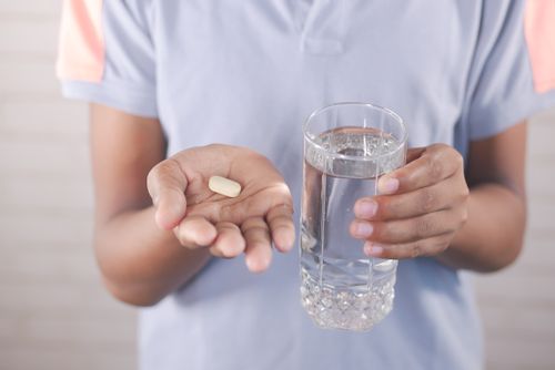 Free Adult holding a pill with a glass of water, ready for medicine consumption. Stock Photo