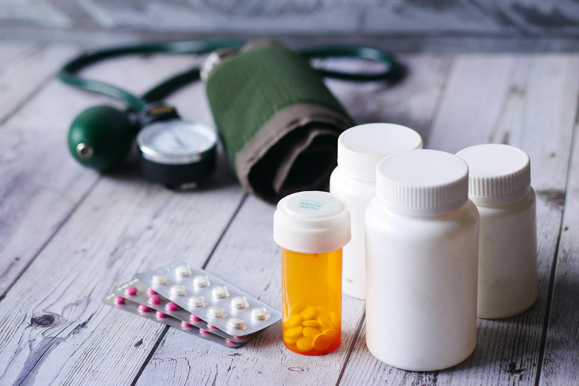 Close-up of medical supplies including pill bottles and a blood pressure monitor on a wooden surface.