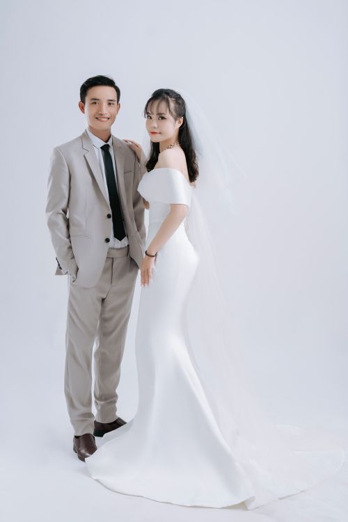 Free A beautiful Asian couple in formal wedding attire posed in a white studio setting. Stock Photo