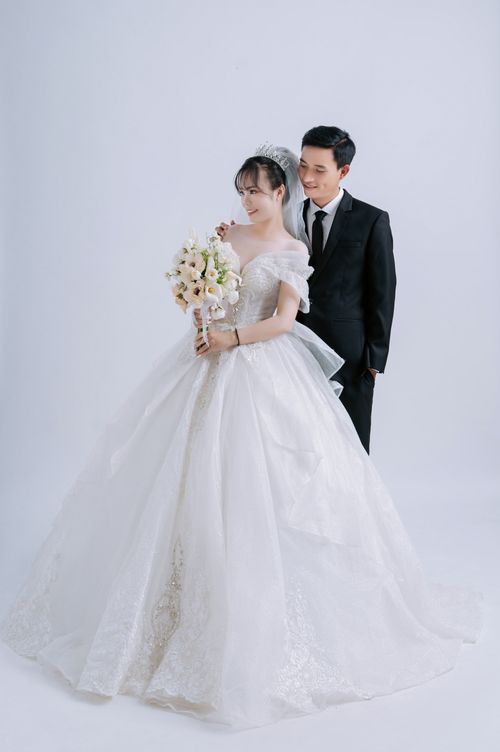 Free A beautiful wedding portrait featuring a smiling couple in formal attire with a bouquet indoors. Stock Photo