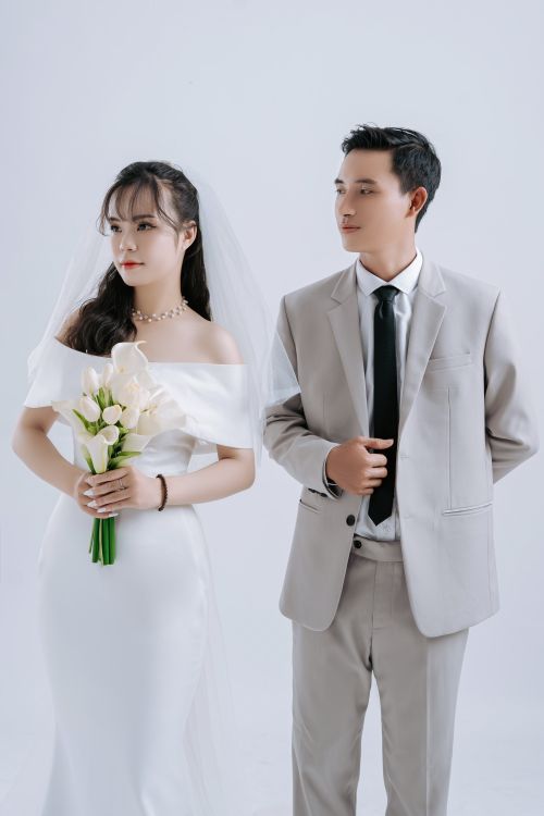 Free Stylish bride and groom in a studio setting, dressed in formal wedding attire with calla lilies. Stock Photo