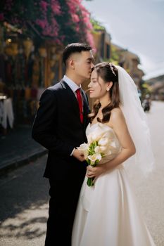 Close-up of a smiling bride and groom sharing a tender moment outdoors with a bouquet.