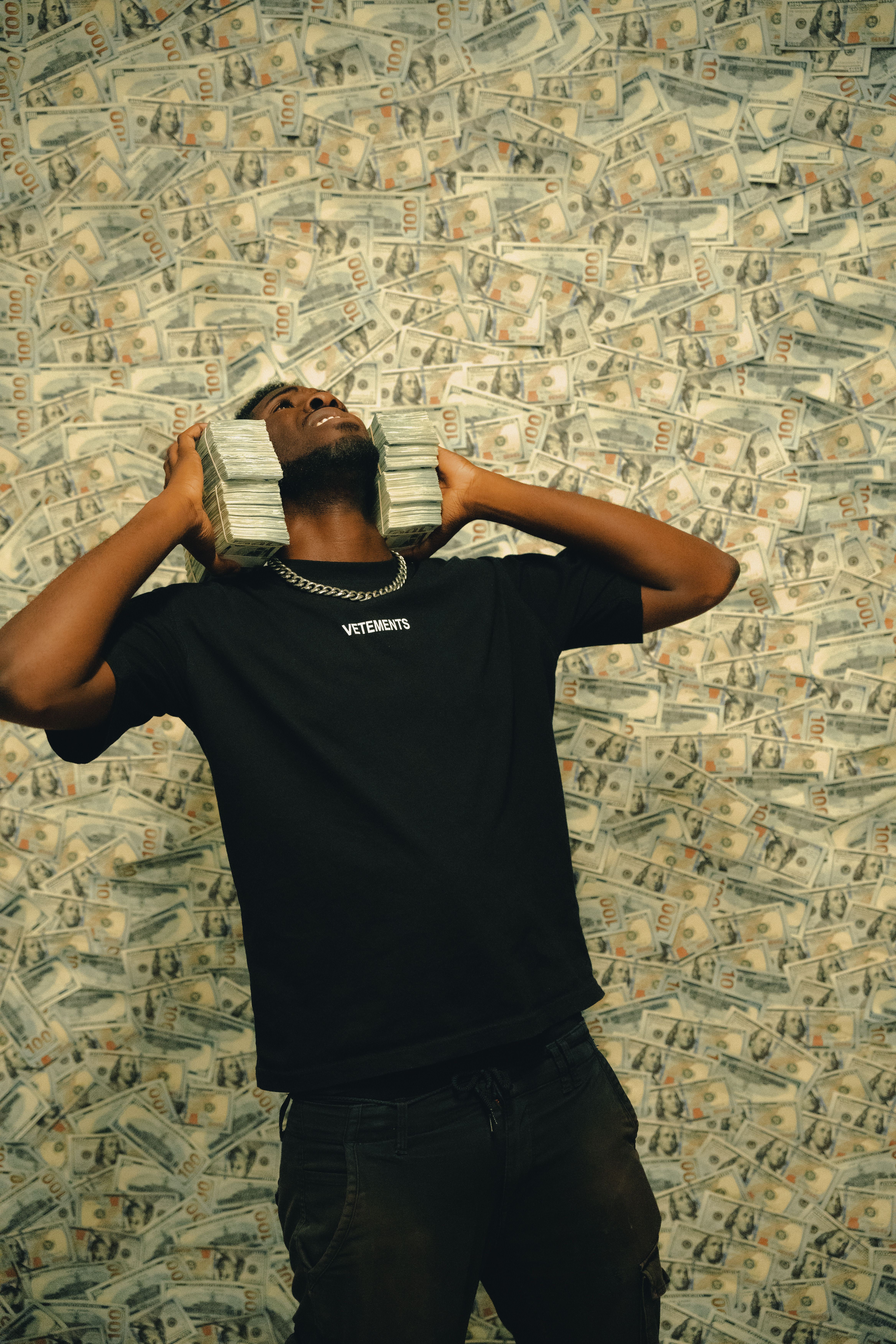 Confident man posing with stacks of dollar bills in front of a cash background.