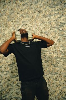 Confident man posing with stacks of dollar bills in front of a cash background.