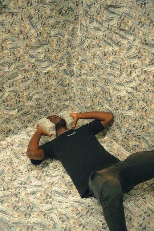 Free A man poses lying on a large pile of dollar bills, holding cash bundles. Conceptual finance imagery. Stock Photo