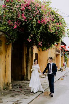 Bride and groom holding hands under vibrant flowers in an idyllic street scene.