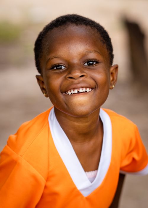 Free Portrait of a smiling African American child in an orange shirt, outdoors. Stock Photo