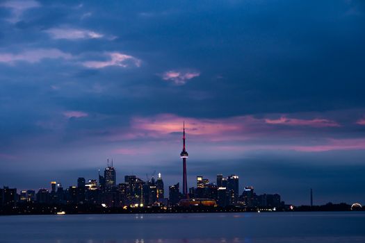 Dramatic view of Toronto's skyline at sunset, featuring the illuminated CN Tower against a vibrant sky.