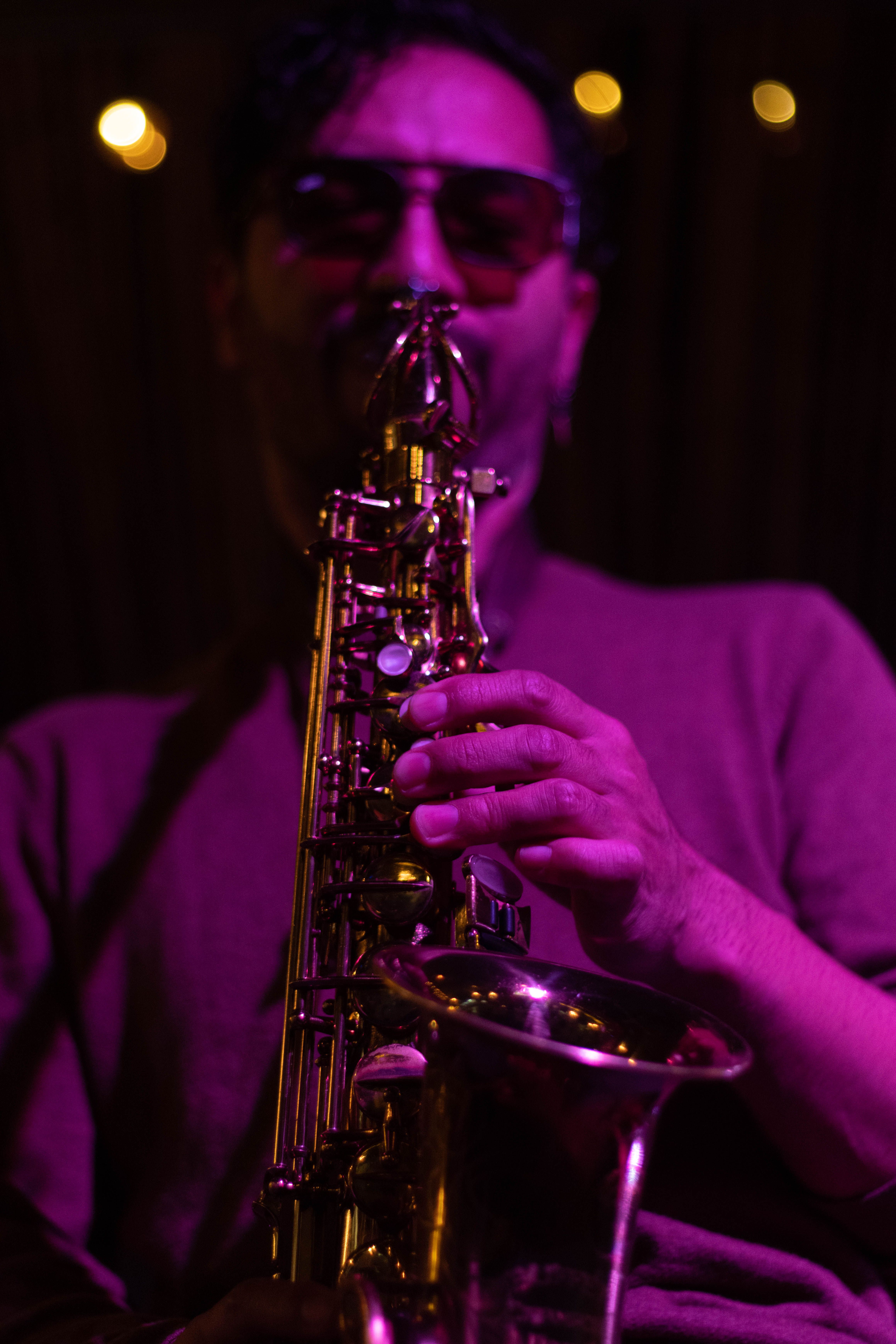 A saxophonist in sunglasses performs jazz music under moody purple lighting.