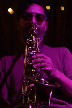 A saxophonist in sunglasses performs jazz music under moody purple lighting.