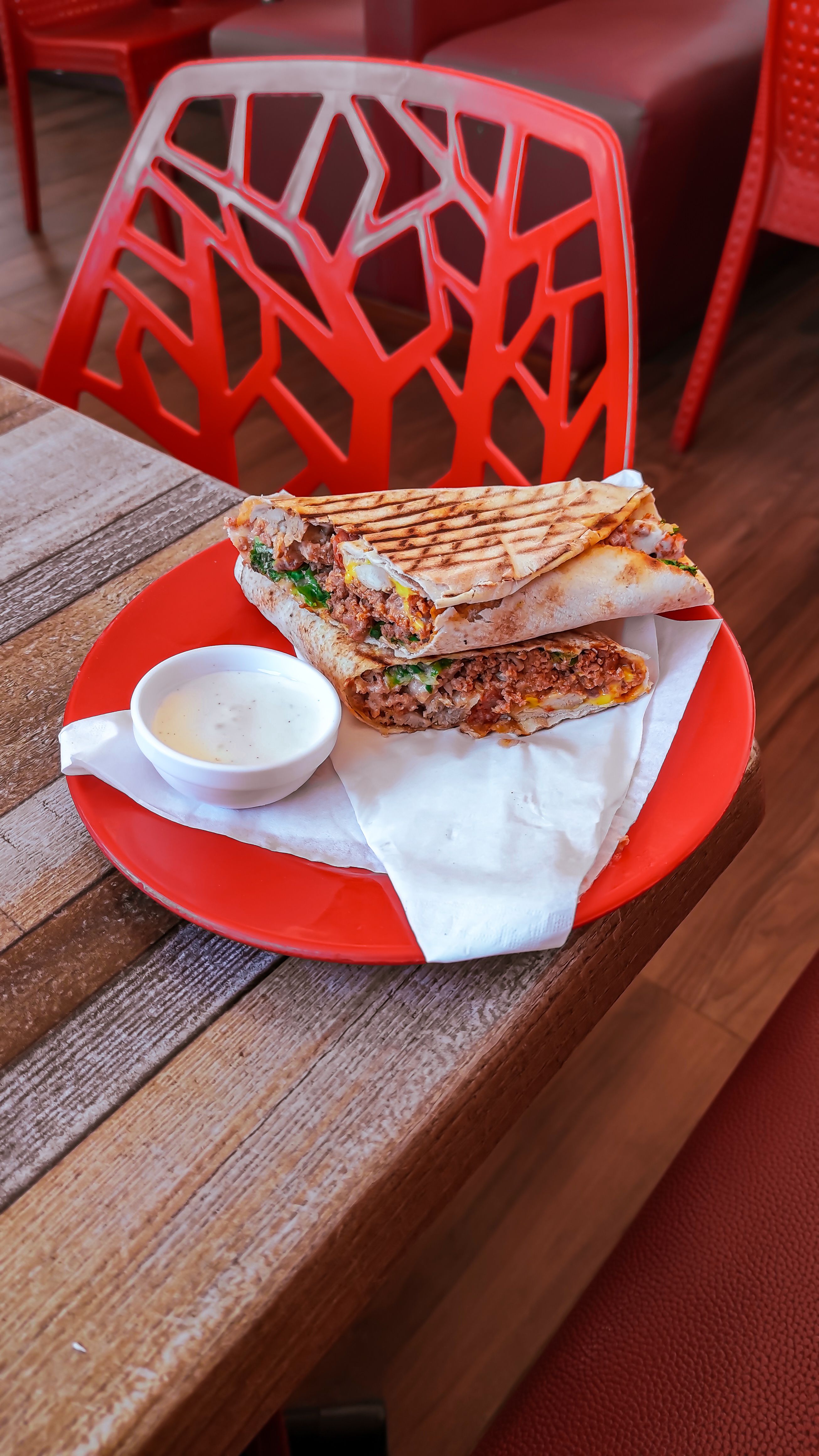 Appetizing burrito with dip served on a vibrant red plate in a cozy cafe interior.