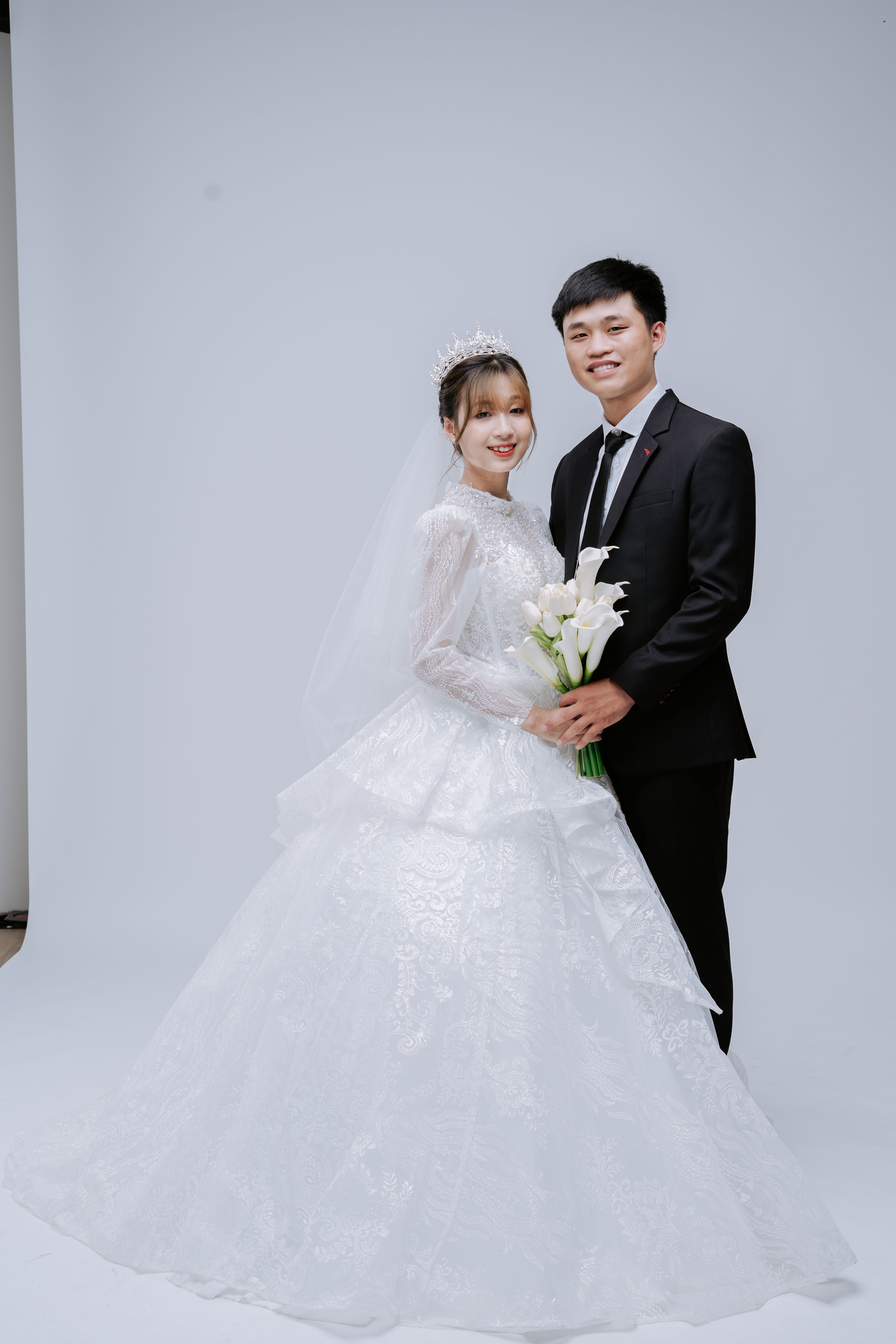A smiling bride and groom in a studio setting wearing elegant wedding attire.